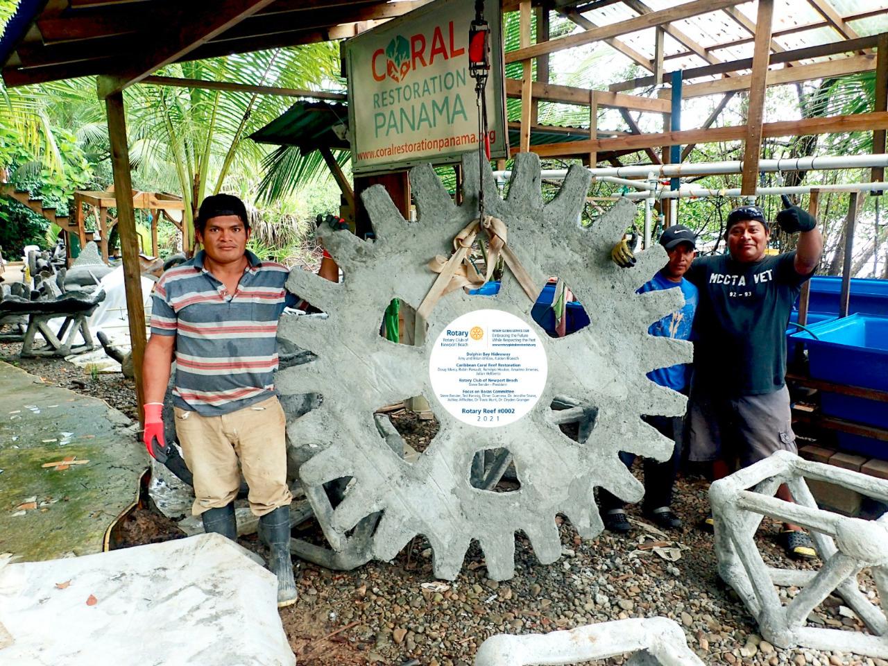Two men stand beside a concrete reef module shaped like the Rotary wheel